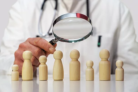 Arzt hält Luppe über Holzfiguren.