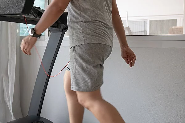 Mensch, der langsam in grauer Trainingskleidung auf dem Laufband zu Hause läuft.