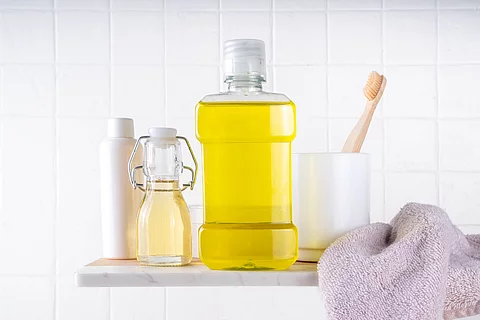 Oil Pulling Mouthwash, dental oral hygiene rinse aid liquid, trendy alternative detoxifying mouthwash with toothbrush, toothpaste for cleaning teeth on bath background Materialien zur Mundpflege, Öl in Mundwasserflasche