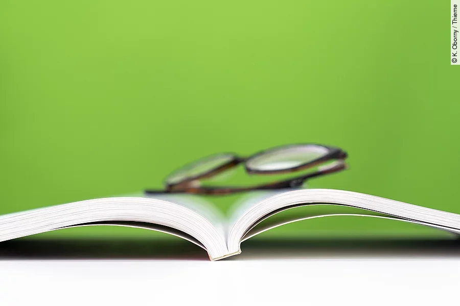 ein aufgeschlagenes Buch, darauf liegt eine Brille