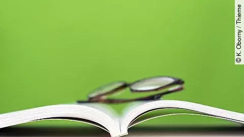 ein aufgeschlagenes Buch, darauf liegt eine Brille
