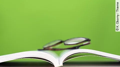 ein aufgeschlagenes Buch, darauf liegt eine Brille