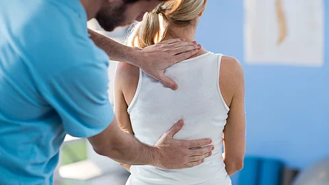 Physiotherapeut behandelt den Rücken einer sitzenden Patientin