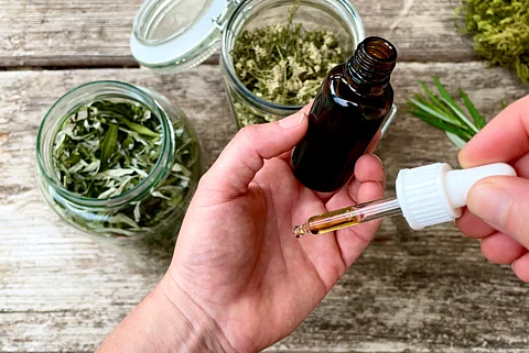 Hand hält Braunfläschchen, darum liegen 