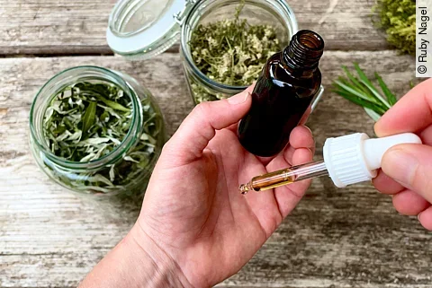 Hand hält Braunfläschchen, darum liegen 