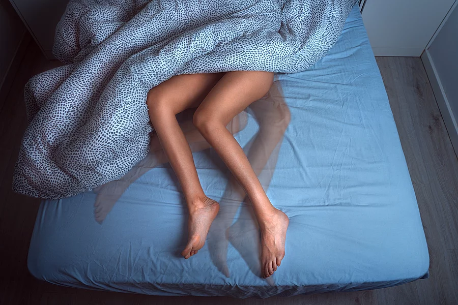 Woman sleeping in the bed and suffering from RLS or restless leg Frau mit Restless Legs Syndrom im Bett