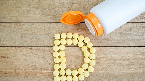 gelbe Pillen als D gelegt auf Holzuntergrund, Symbolbild für Vitamin D