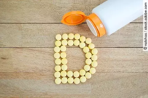 gelbe Pillen als D gelegt auf Holzuntergrund, Symbolbild für Vitamin D