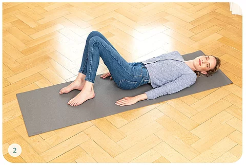 Junge Frau in Alltagskleidung macht Übungen auf Yogamatte 