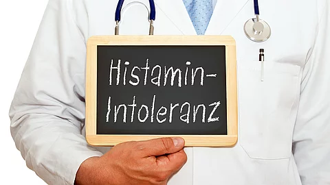 Arzt hält Kreidetafel mit dem Text Histamin Intoleranz vor seinem Kittel in der Hand
