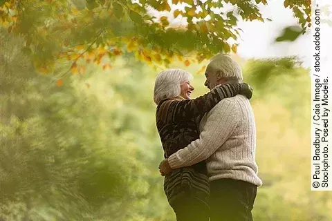 Älteres Paar, das sich lachend umarmt, in einem herbstlichen Wald oder Park Älteres Paar, das sich lachend umarmt, in einem herbstlichen Wald oder Park