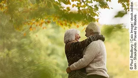Älteres Paar, das sich lachend umarmt, in einem herbstlichen Wald oder Park