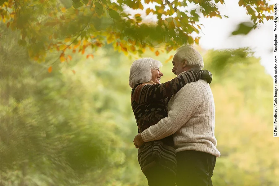 Älteres Paar, das sich lachend umarmt, in einem herbstlichen Wald oder Park