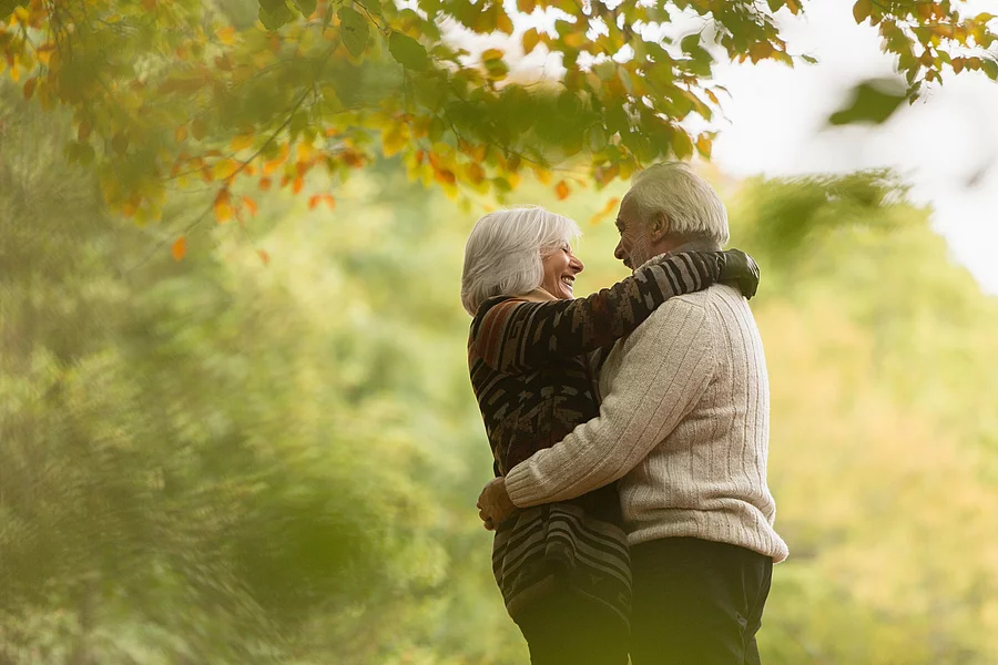 Älteres Paar, das sich lachend umarmt, in einem herbstlichen Wald oder Park