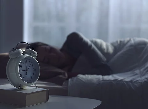 Frau schläft im Bett mit Wecker auf dem Nachttisch.