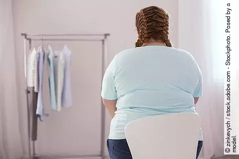 Übergewichtige Frau sitzt auf einem Stuhl mit dem Rücken zur Kamera.