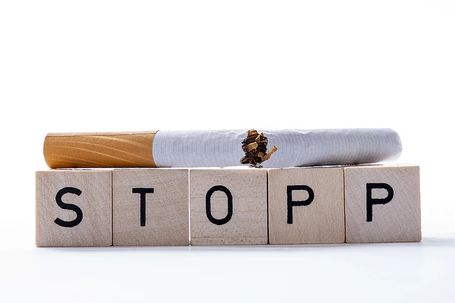 Zerbrochene Zigrarette liegt auf Spielwürfeln mit dem Wort STOPP