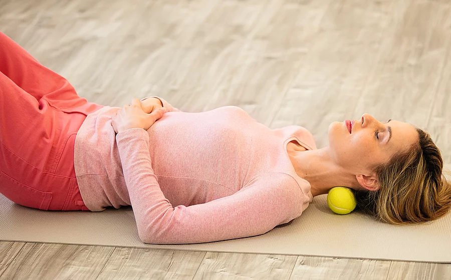 Frau mit Massageball im Nacken liegt auf dem Rücken in Entspannungslage
