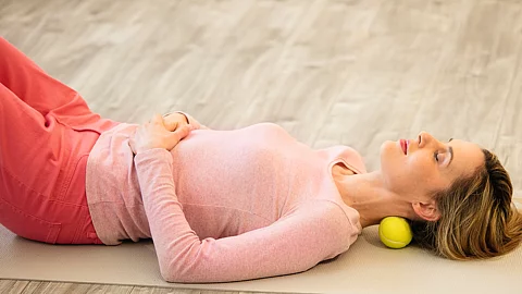Frau mit Massageball im Nacken liegt auf dem Rücken in Entspannungslage