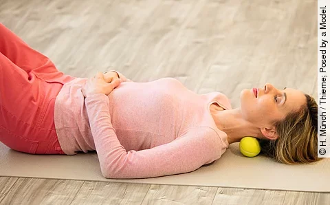 Frau mit Massageball im Nacken liegt auf dem Rücken in Entspannungslage