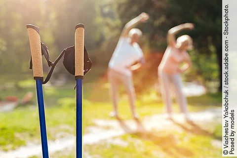 Senioren machen Dehnübungen im Park. Im Vordergrund stehen Wanderstöcke.