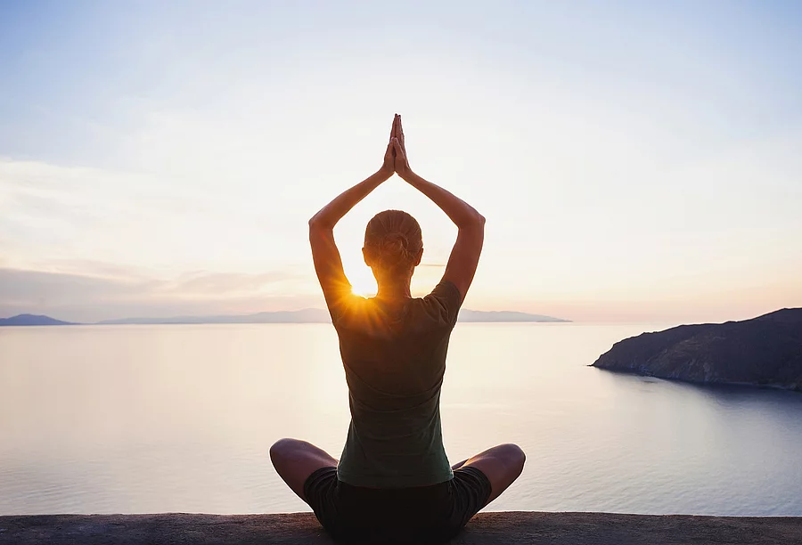 Frau sitzt am Seeufer und macht Yoga.