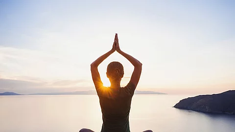 Frau sitzt am Seeufer und macht Yoga.