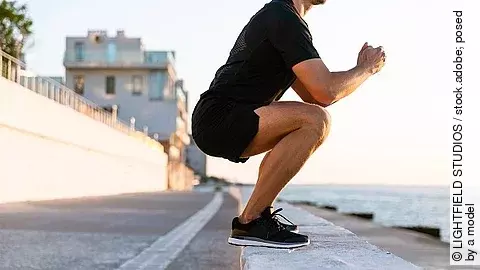 Sportler in der Kniebeuge an einer Uferpromenade