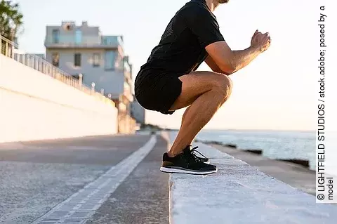 Sportler in der Kniebeuge an einer Uferpromenade