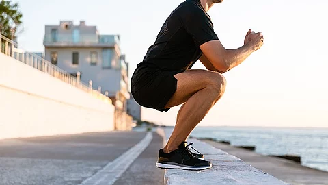 Sportler in der Kniebeuge an einer Uferpromenade