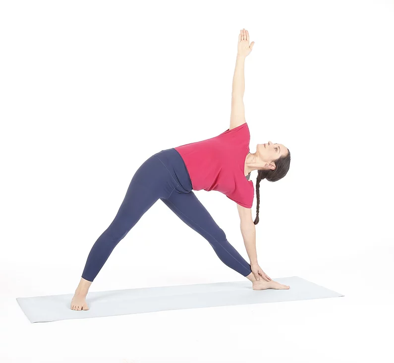 Frau praktiziert Trikonoasana mit nach unten und oben gestreckten Armen