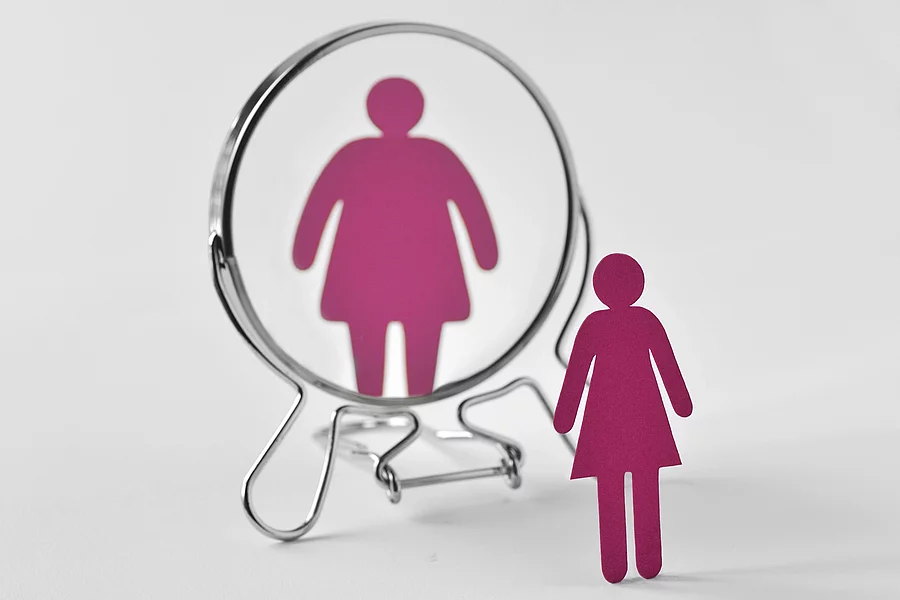 Slim paper woman looking in the mirror and seeing herself as a f Papierfrau schaut sich im Spiegel an, sieht sich dicker als in der Realität
