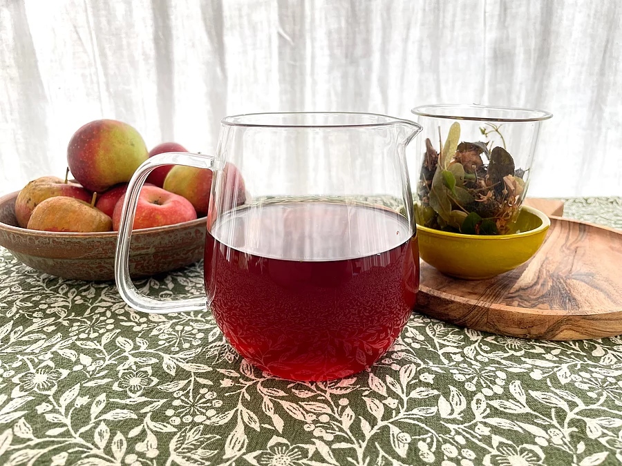 Gläserne Teekanne mit dunklem Kräutertee auf Steintisch