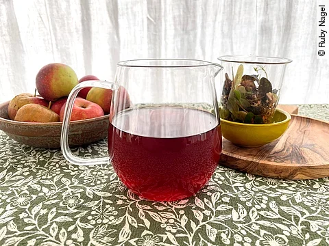 Gläserne Teekanne mit dunklem Kräutertee auf Steintisch