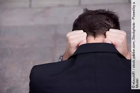 Mann ist mit dem Rücken zugewandt und hält seinen Kopf mit beiden Armen fest.