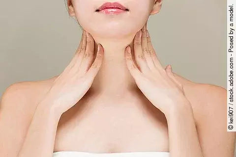 Junge Frau streicht sich mit beiden Händen über den Hals.