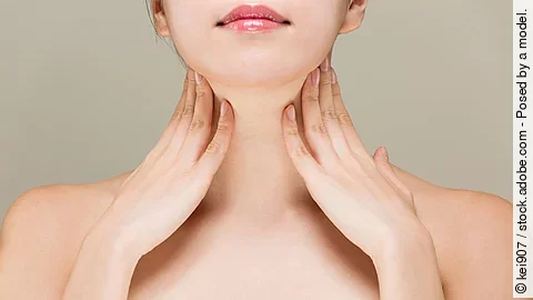 Junge Frau streicht sich mit beiden Händen über den Hals.