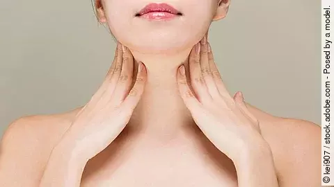 Junge Frau streicht sich mit beiden Händen über den Hals.