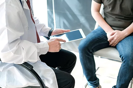 Arzt hält ein iPad und berät einen Patienten (beide sitzend).