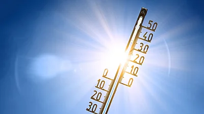 Thermometer vor blauem Himmel und Sonne