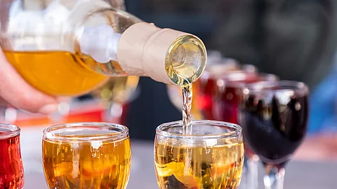 Aus einer Flasche wird Wein in ein Glas eingeschenkt. Im Hintergrund sind weitere befüllte Weingläser zu sehen.