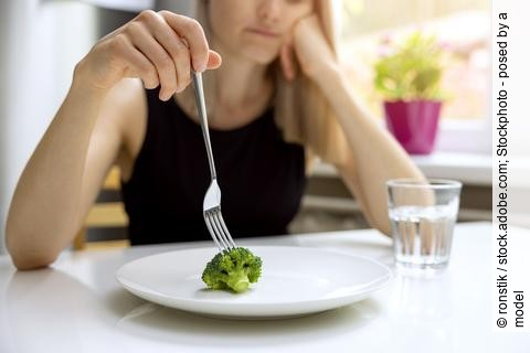 Essstörung, junge Frau stochert auf einem Teller mit einem kleinen Broccolo-Röschen