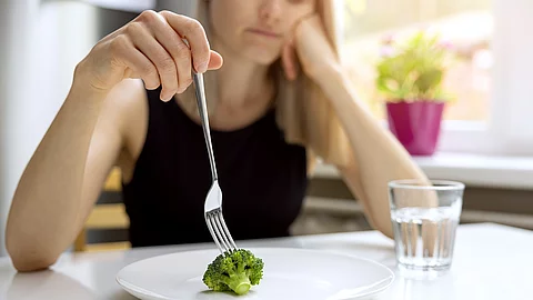 dieting problems, eating disorder - unhappy woman looking at sma Essstörung, junge Frau stochert auf einem Teller mit einem kleinen Broccolo-Röschen