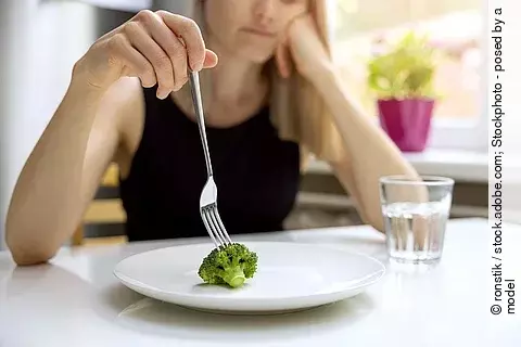 Essstörung, junge Frau stochert auf einem Teller mit einem kleinen Broccolo-Röschen
