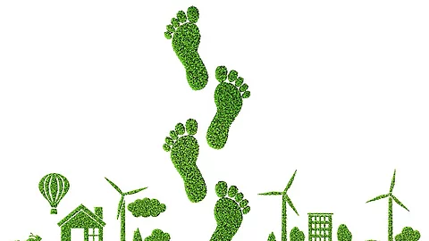 Illustration CO2-Fußabdruck. In der Mitte sind grüne Fußabdrücke. Links und rechts sind Häuser, Bäume, Windräder.