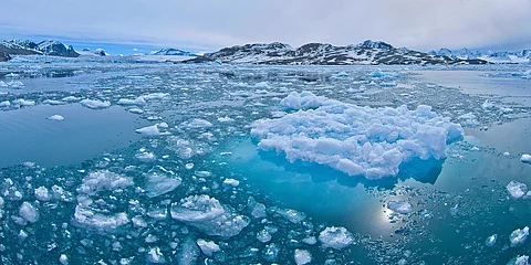Eisschollen treiben auf dem Wasser. Im Hintergrund sind Erhebungen.