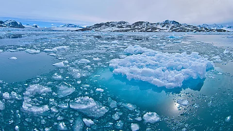 Eisschollen treiben auf dem Wasser. Im Hintergrund sind Erhebungen.