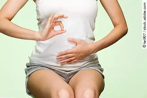 Frau in weißem Top, die sich die Darmgegend hält.