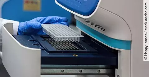 Eine Hand mit blauem Handschuh setzt Proben in eine PCR-Maschine ein.