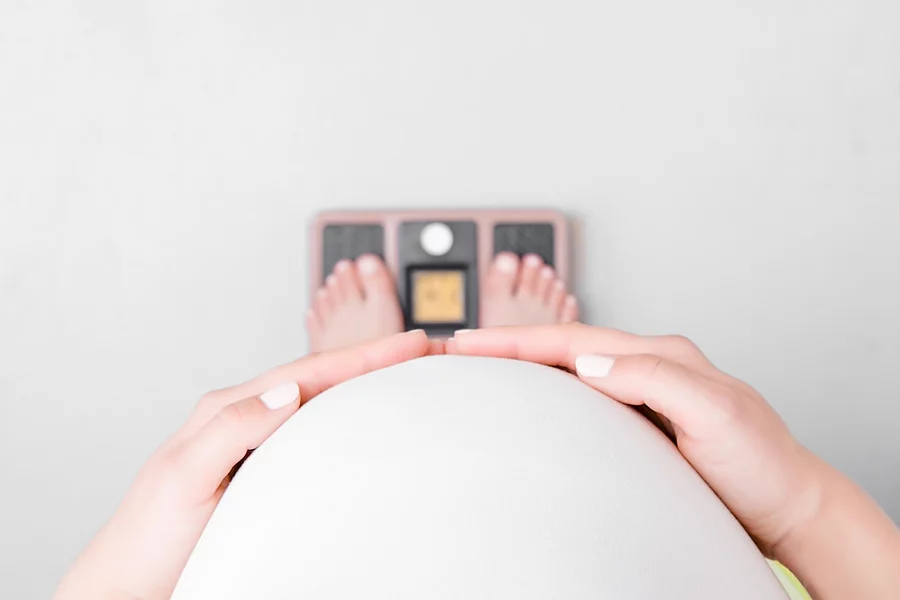 Young pregnant woman with barefoot standing on weight scales. Ca schwangere Frau steht auf der Waage